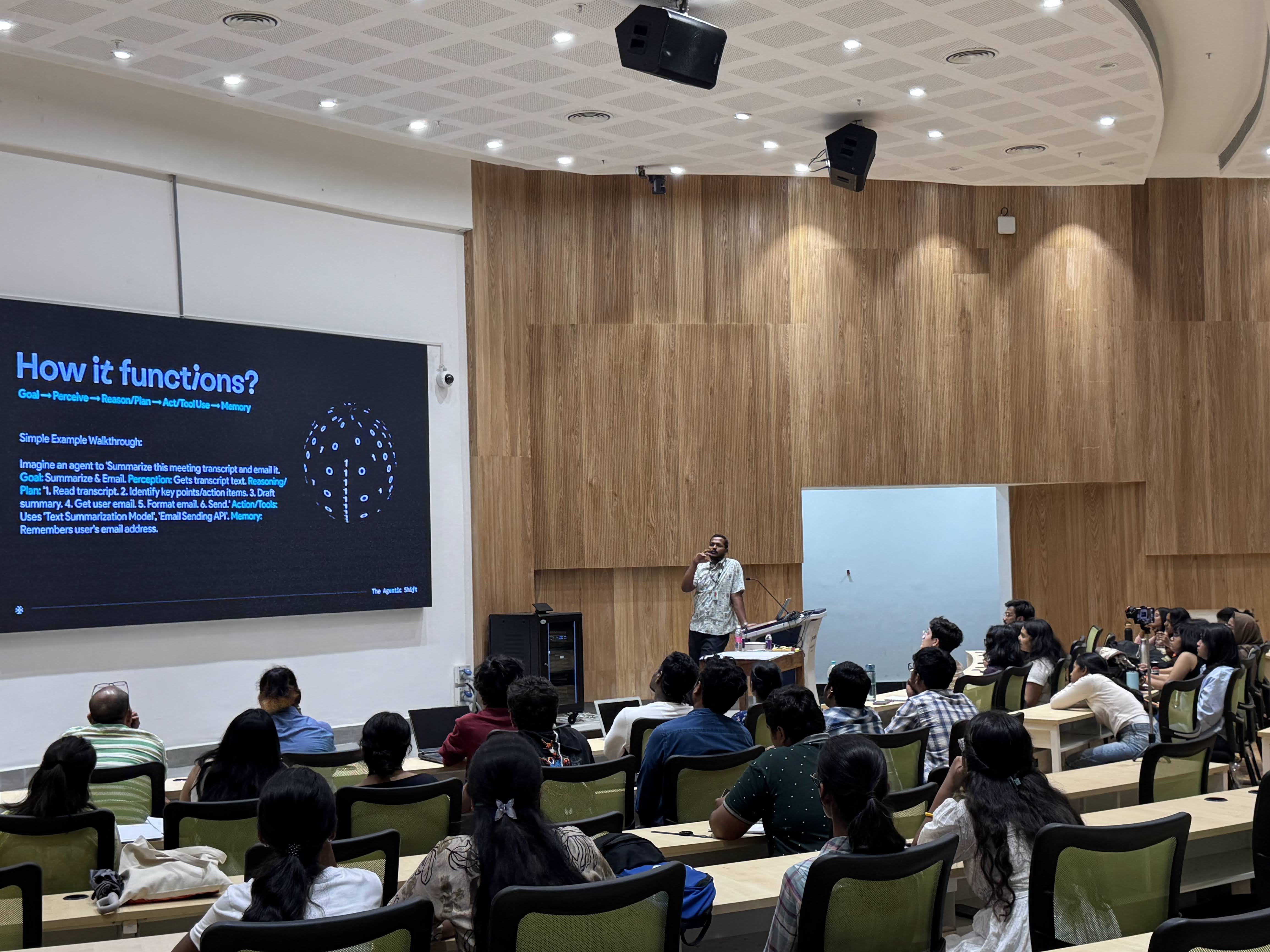 Tejj lecturing on AI agent architecture in a university auditorium